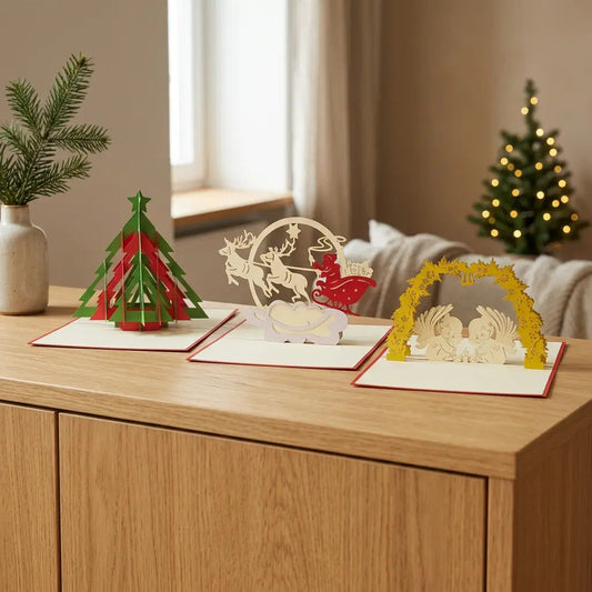 Drei geöffnete Pop-Up-Weihnachtskarten mit Tannenbaum, Weihnachtsmann im Rentierschlitten und Engeln auf einem Eichensideboard, mit beleuchtetem Weihnachtsbaum im Hintergrund.