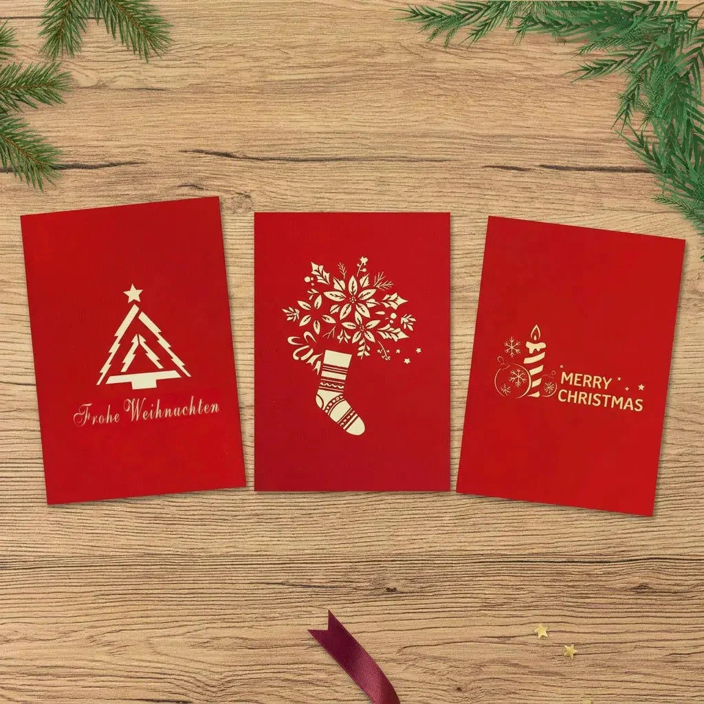 Drei rote Weihnachtskarten mit modernem Tannenbaum, blumengeschmücktem Weihnachtsstrumpf und Kerzenmotiv auf einem hellen Holztisch.