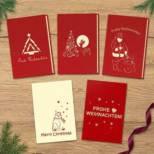 Fünf geschlossene Weihnachtskarten mit Tannenbaum, Baum und Rentier, Weihnachtsmann, Eisbär und Weihnachtsgruß auf einem festlich dekorierten Holztisch.