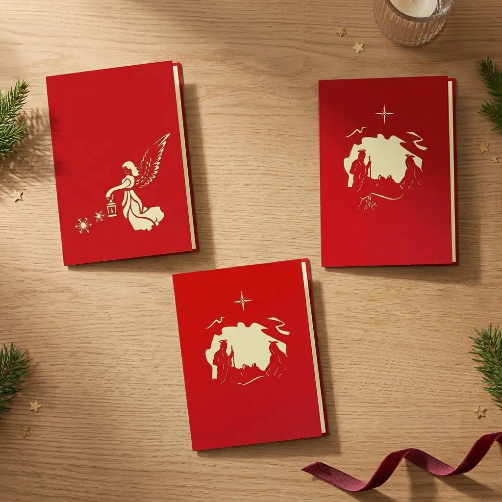 Drei geschlossene rote Weihnachtskarten des Sets Weihnachtssegen mit Engel-, Stern- und Krippenmotiv auf einem festlichen Holztisch.