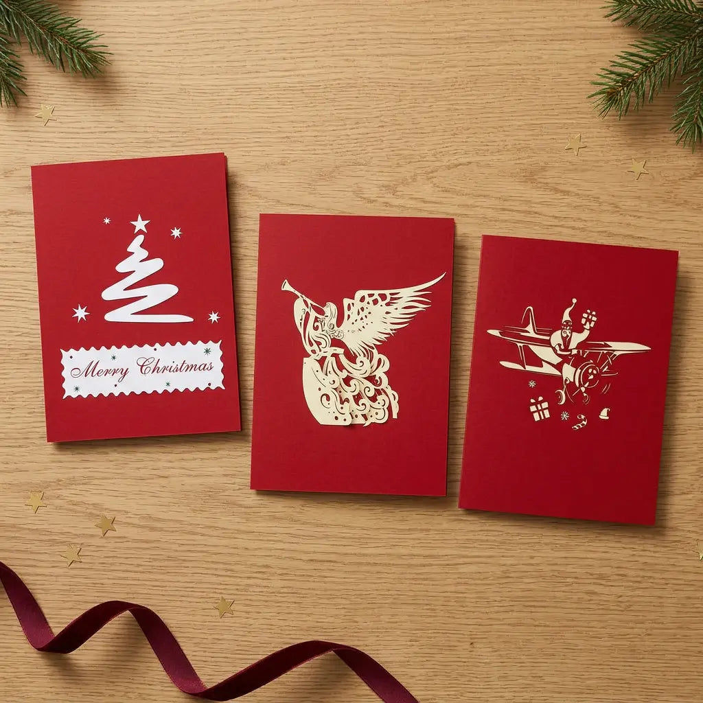 Drei rote Weihnachtskarten mit Tannenbaum, trompetenspielendem Engel und Nikolaus im Doppeldecker auf einem festlich dekorierten Holztisch.