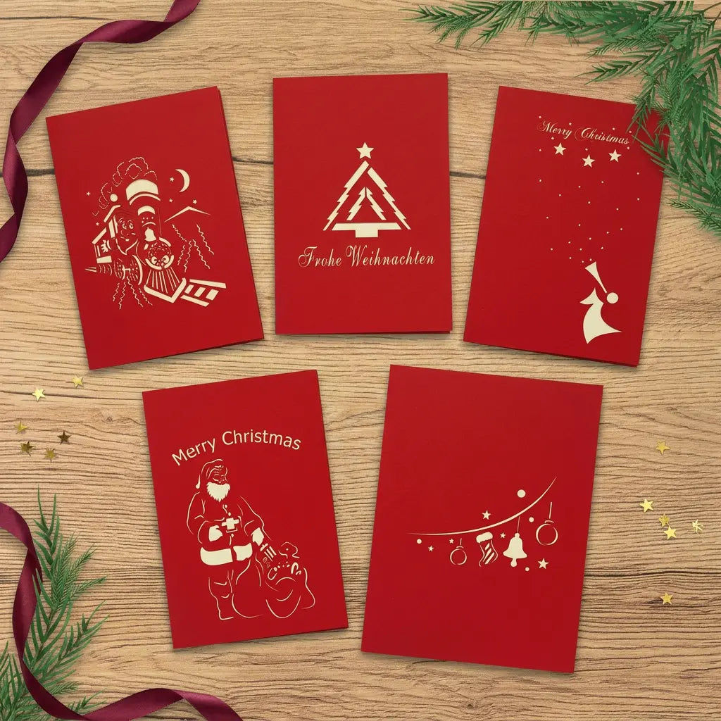 Fünf rote Weihnachtskarten mit Tannenbaum, Weihnachtszug, Engel, Weihnachtsmann und Ornamentgirlande auf einem festlich dekorierten Holztisch.
