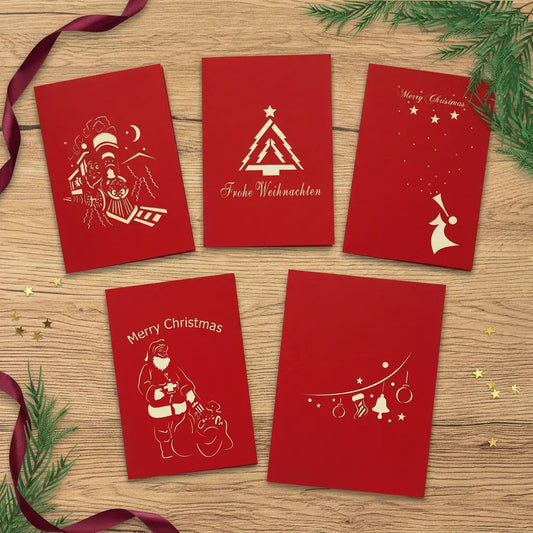 Fünf rote Weihnachtskarten mit Tannenbaum, Weihnachtszug, Engel, Weihnachtsmann und Ornamentgirlande auf einem festlich dekorierten Holztisch.
