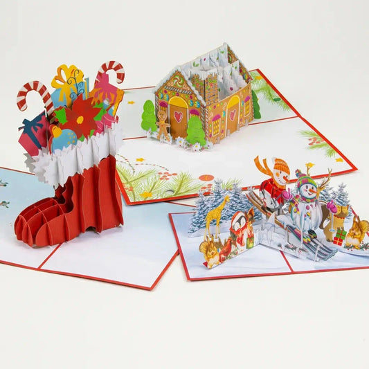 Drei geöffnete LINPopUp 3D Pop-Up-Weihnachtskarten im Set Gemütliche Weihnachten: Nikolausstiefel mit Geschenken, Lebkuchenhaus und Schneemänner auf Ski.