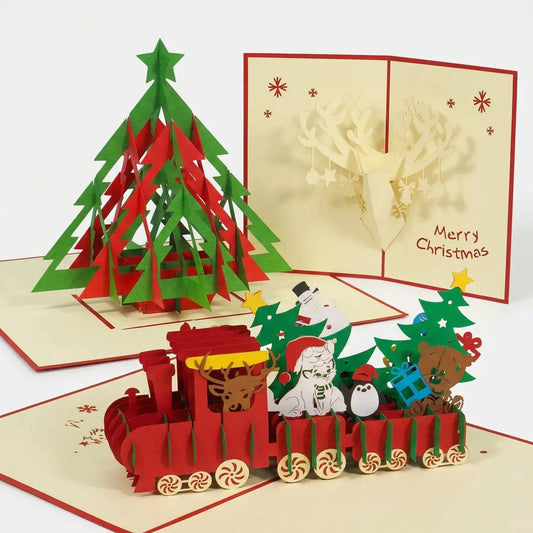 Drei geöffnete LINPopUp Pop-Up-Weihnachtskarten mit rot-grünem Tannenbaum, buntem Weihnachtszug und Rentierkopf mit geschmücktem Geweih