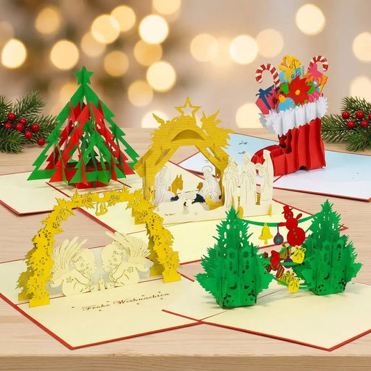 Fünf geöffnete LINPopUp Pop-Up-Weihnachtskarten mit Tannenbäumen, Nikolausstiefel, Engeln und Weihnachtskrippe auf hellem Holz vor warmen Weihnachtslichtern