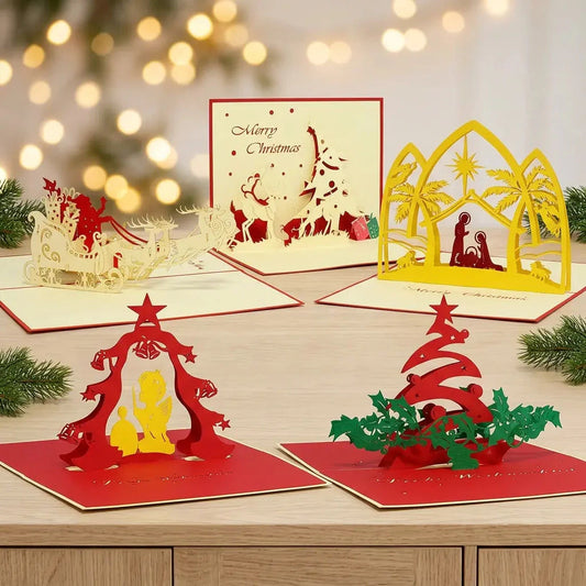 Fünf geöffnete Pop-Up-Weihnachtskarten des Sets Weihnachtsmomente mit Rentierschlitten, Krippe, Rentier und zwei roten Baummotiven auf einem Holztisch vor Weihnachtslichtern
