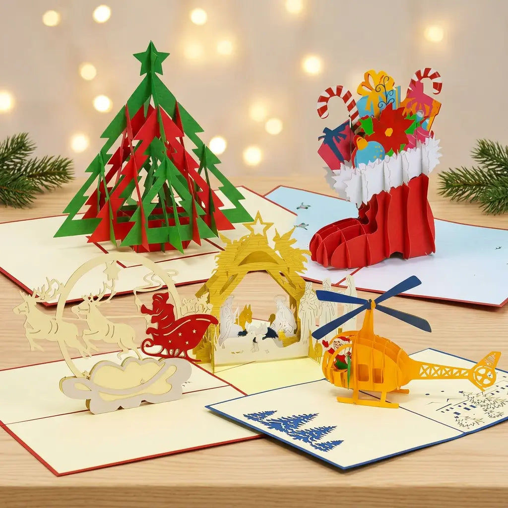Fünf geöffnete LINPopUp Pop-Up-Weihnachtskarten mit Tannenbaum, Nikolausstiefel, Rentierschlitten, Krippe und Helikopter auf hellem Holz vor warmen Weihnachtslichtern