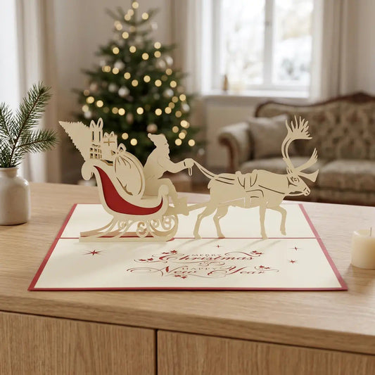 Geöffnete Pop-Up-Weihnachtskarte mit cremefarbenem Weihnachtsmann im rot verzierten Schlitten und einem Rentier auf einem Eichensideboard vor einem beleuchteten Weihnachtsbaum.