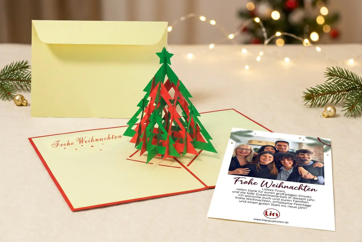 Geöffnete 3D-Pop-up-Weihnachtskarte mit rot-grünem Tannenbaum, passendem Umschlag und separatem Einleger mit Teamfoto und Weihnachtsgruß auf einem festlich dekorierten Tisch.